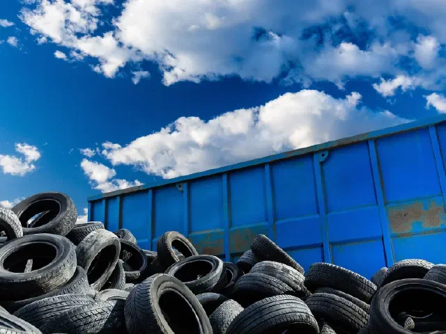 Llantas usadas apiladas junto a un contenedor de reciclaje